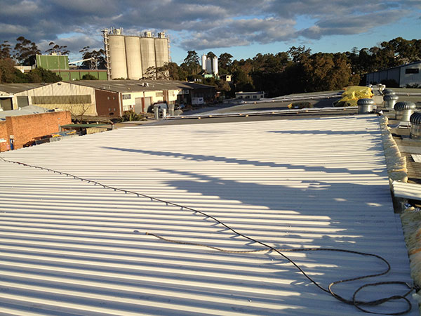 industrial roof with white metal sheets and buildings silos in the background under a cloudy sky