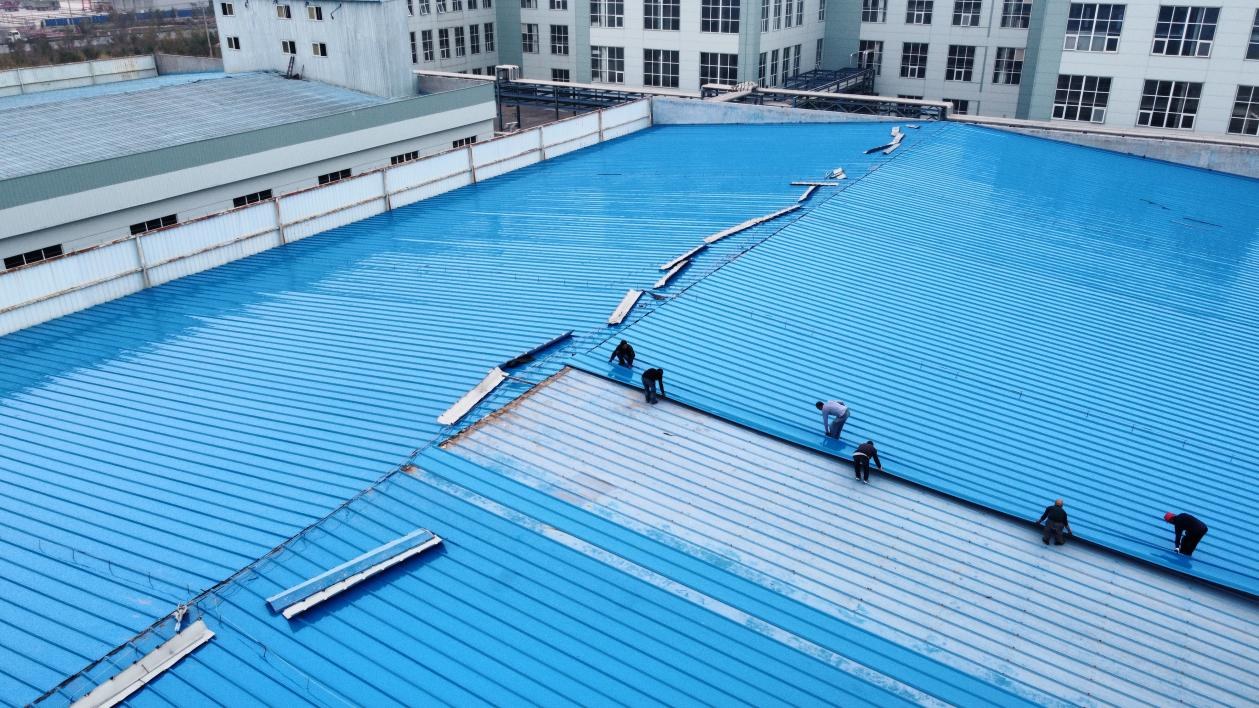 Workers installing or repairing a blue metal roof on an industrial building